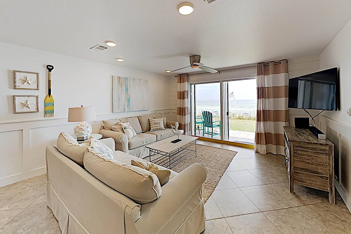 A living room with a sofa, a coffee table, a TV, and a view of the ocean through large sliding doors.