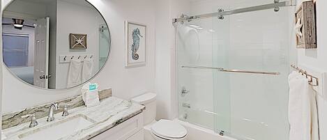 A modern bathroom with a marble vanity, a glass shower enclosure, and a large mirror.