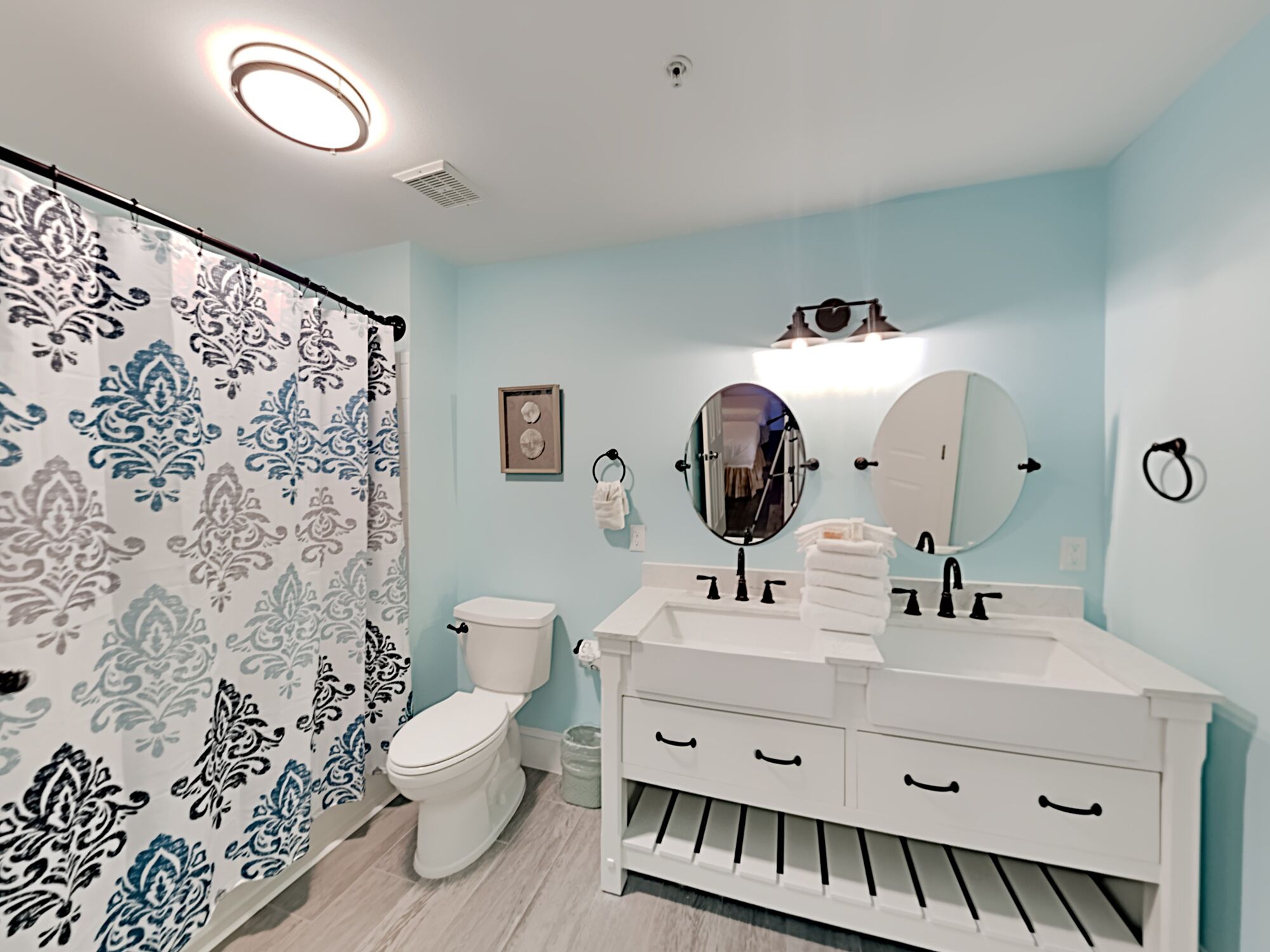 Une salle de bain comprenant des toilettes, un lavabo avec deux miroirs et un rideau de douche à motifs floraux.