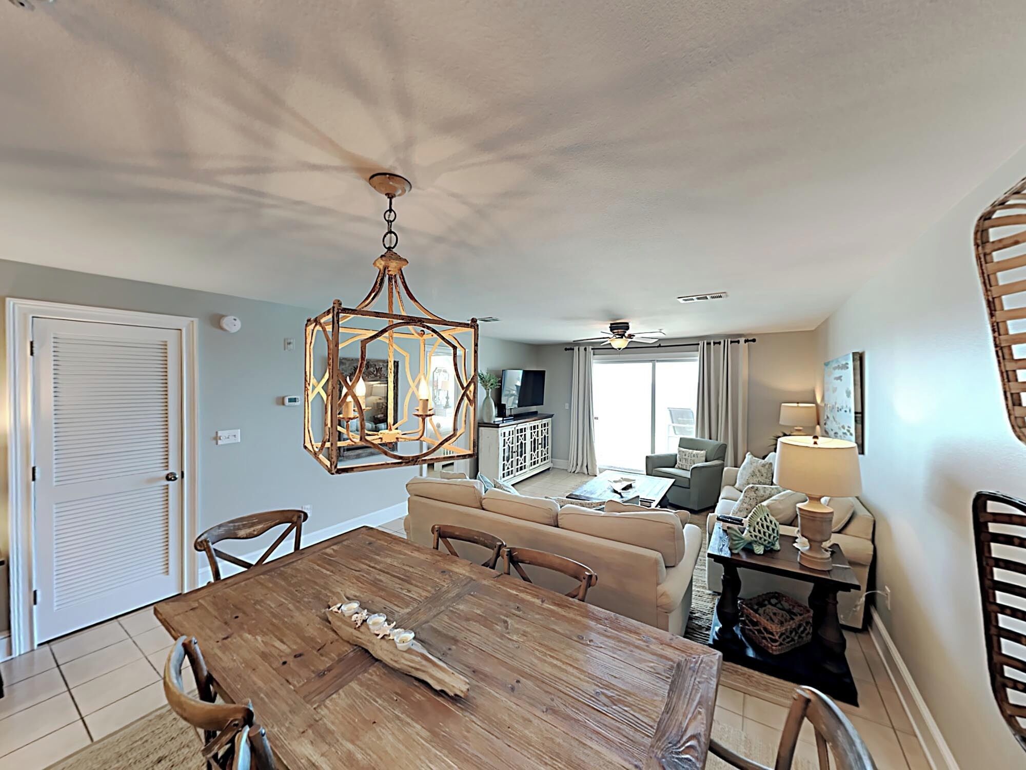 A dining area with a wooden table and chairs, a chandelier, and a sofa in the background.