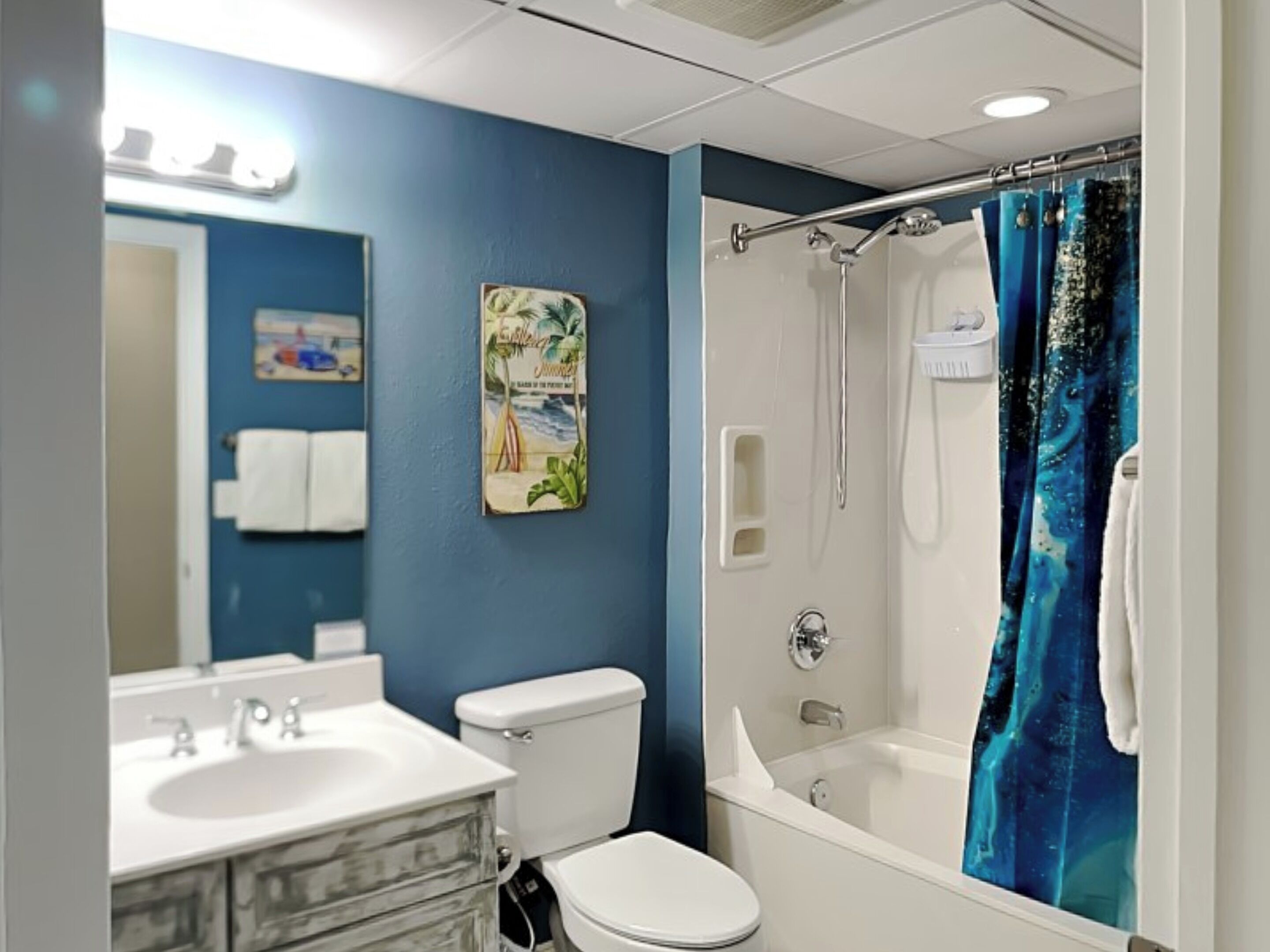 Un bagno con lavandino, water e vasca da bagno bianchi. Si nota una tenda blu per la doccia e un portascope.