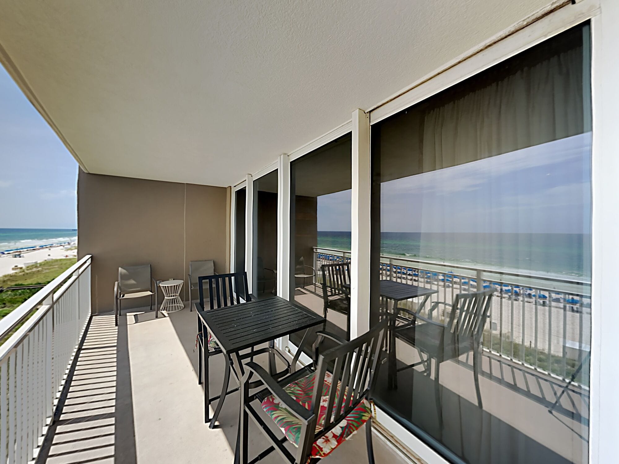 A balcony with a table and chairs, overlooking a beach.