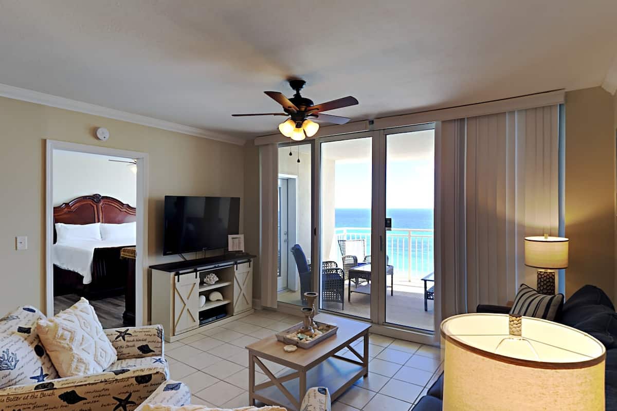 Quarto de hotel com varanda, televisão, sofá, mesa de centro e abajur.