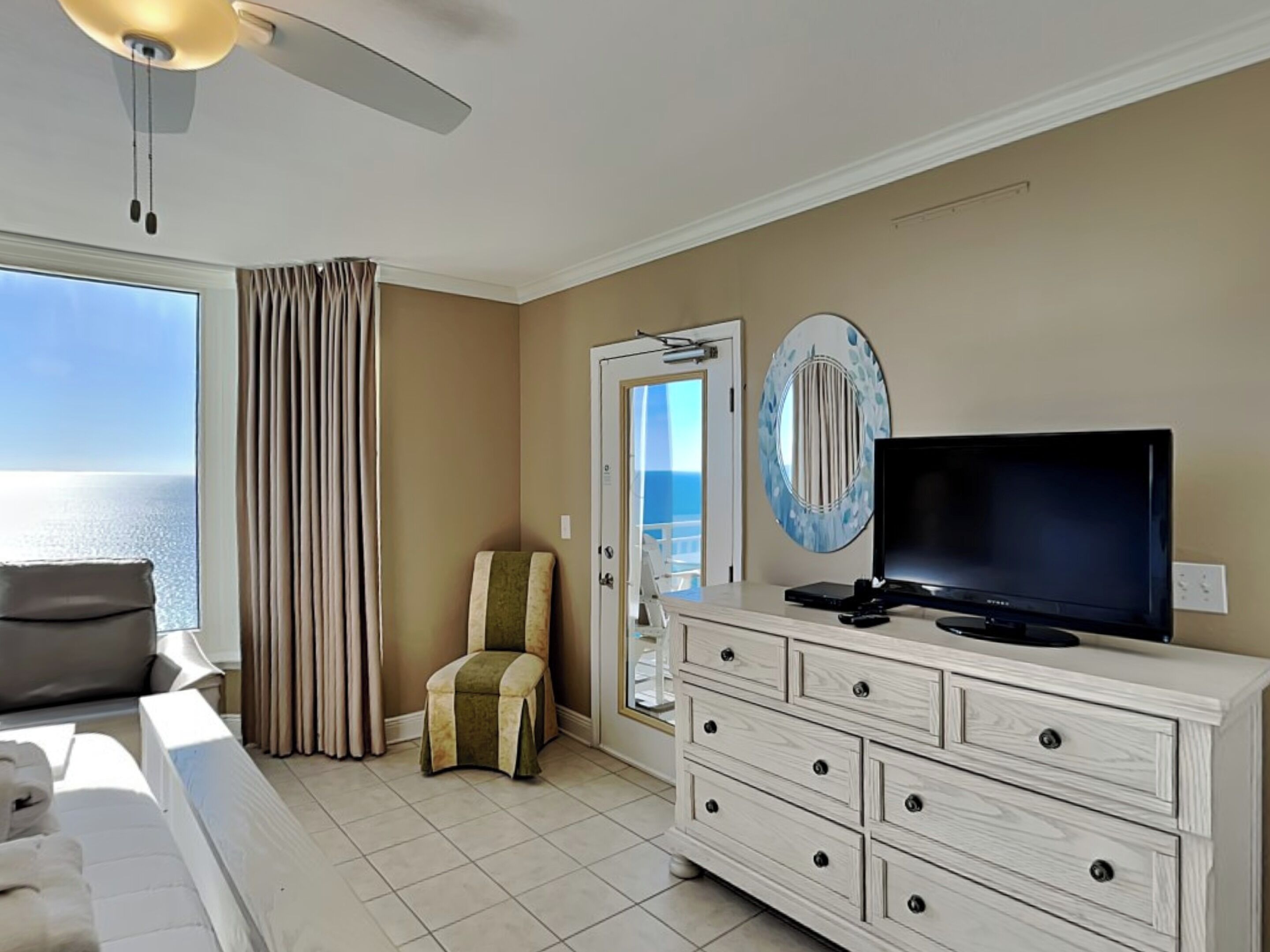 Habitación de hotel con cama, televisor, cómoda, silla y vista al océano.