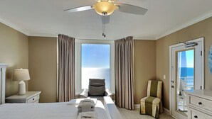 A hotel room with a bed, a chair, a desk, a lamp, and a view of the sea. - Emerald Beach by Southern Vacation Rentals (Panama City Beach)