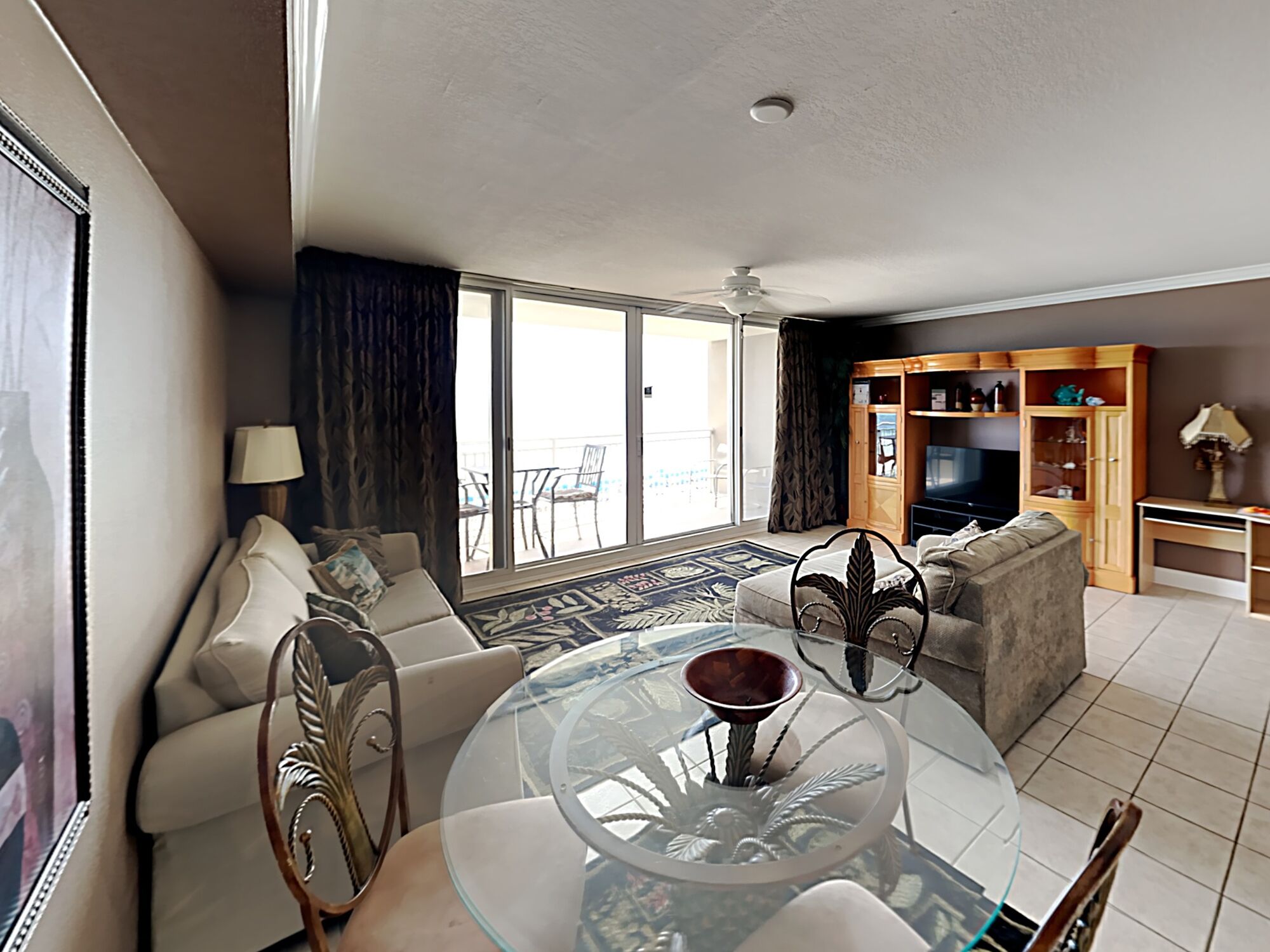 Un salón con una mesa de centro de vidrio, un sofá, un mueble para televisión y un balcón con vistas.