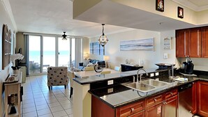 A spacious kitchen with a large island, a dining area with a sofa, and a view of the ocean through large windows. - Emerald Beach by Southern Vacation Rentals (Panama City Beach)