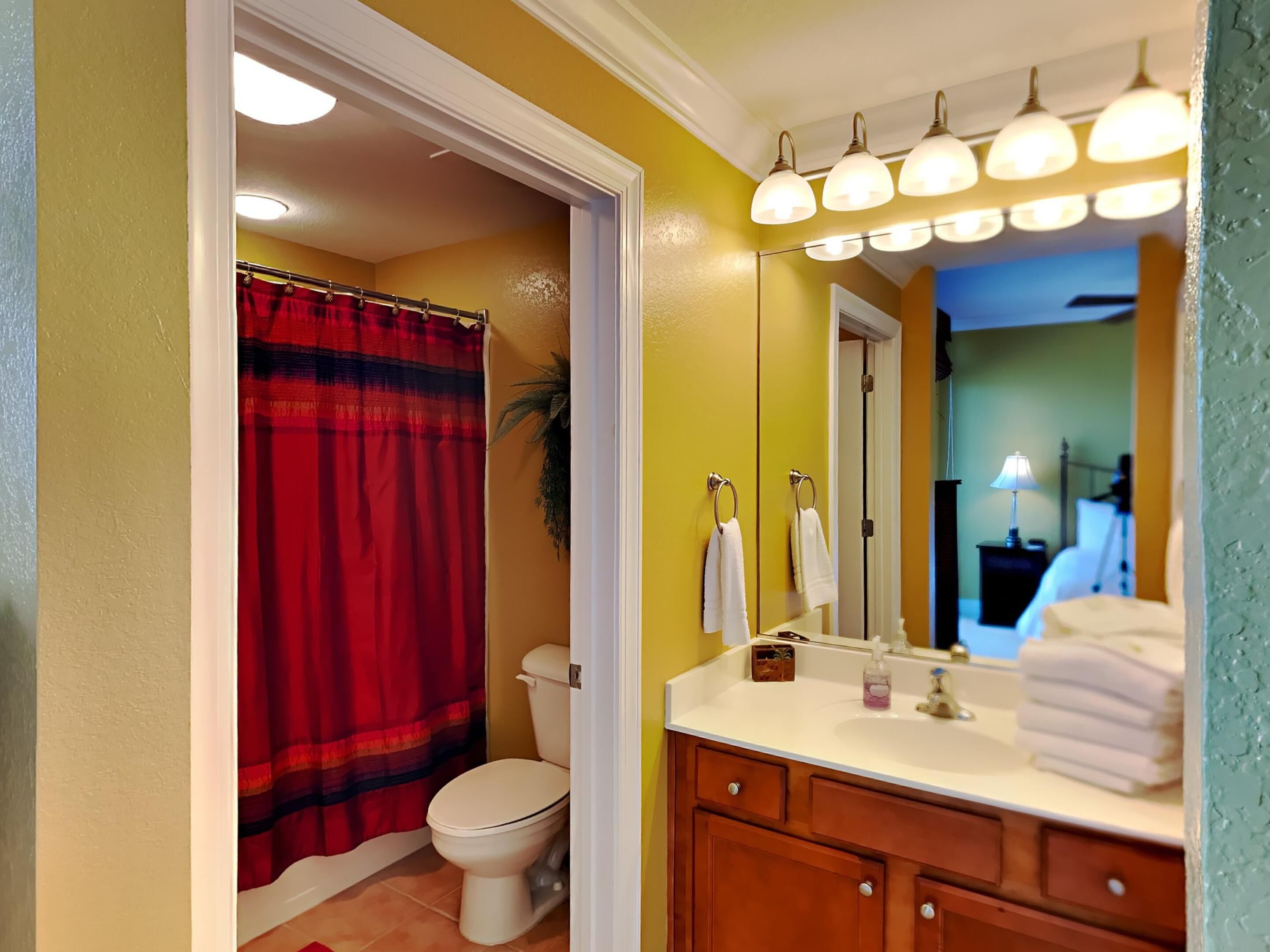 A bathroom with a red shower curtain, white toilet, and a vanity with a mirror and towel rack.