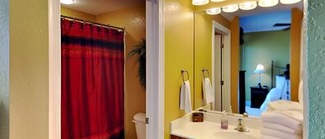 A bathroom with a red shower curtain, white toilet, and a vanity with a mirror and towel rack.