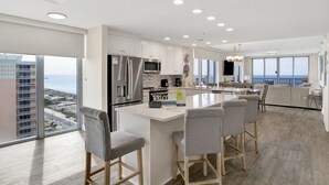 Une cuisine moderne dotée d’un grand îlot central, d’appareils électroménagers en acier inoxydable et offrant une vue sur l’océan.