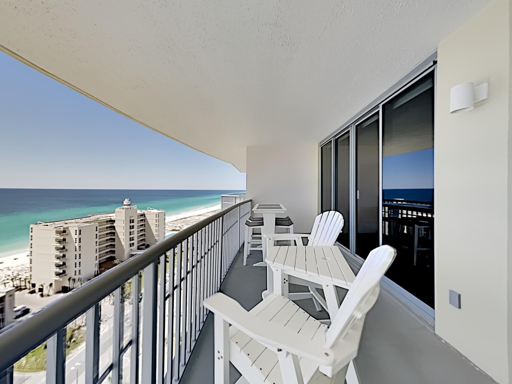 A balcony with a table and chairs, overlooking a beach and buildings.