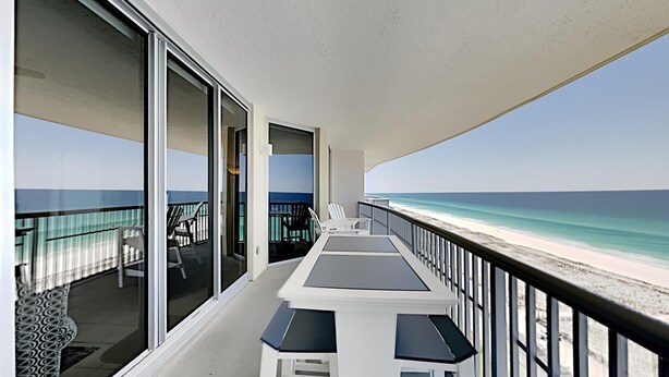 Un balcon donnant sur la plage, une table avec des chaises et une rambarde.