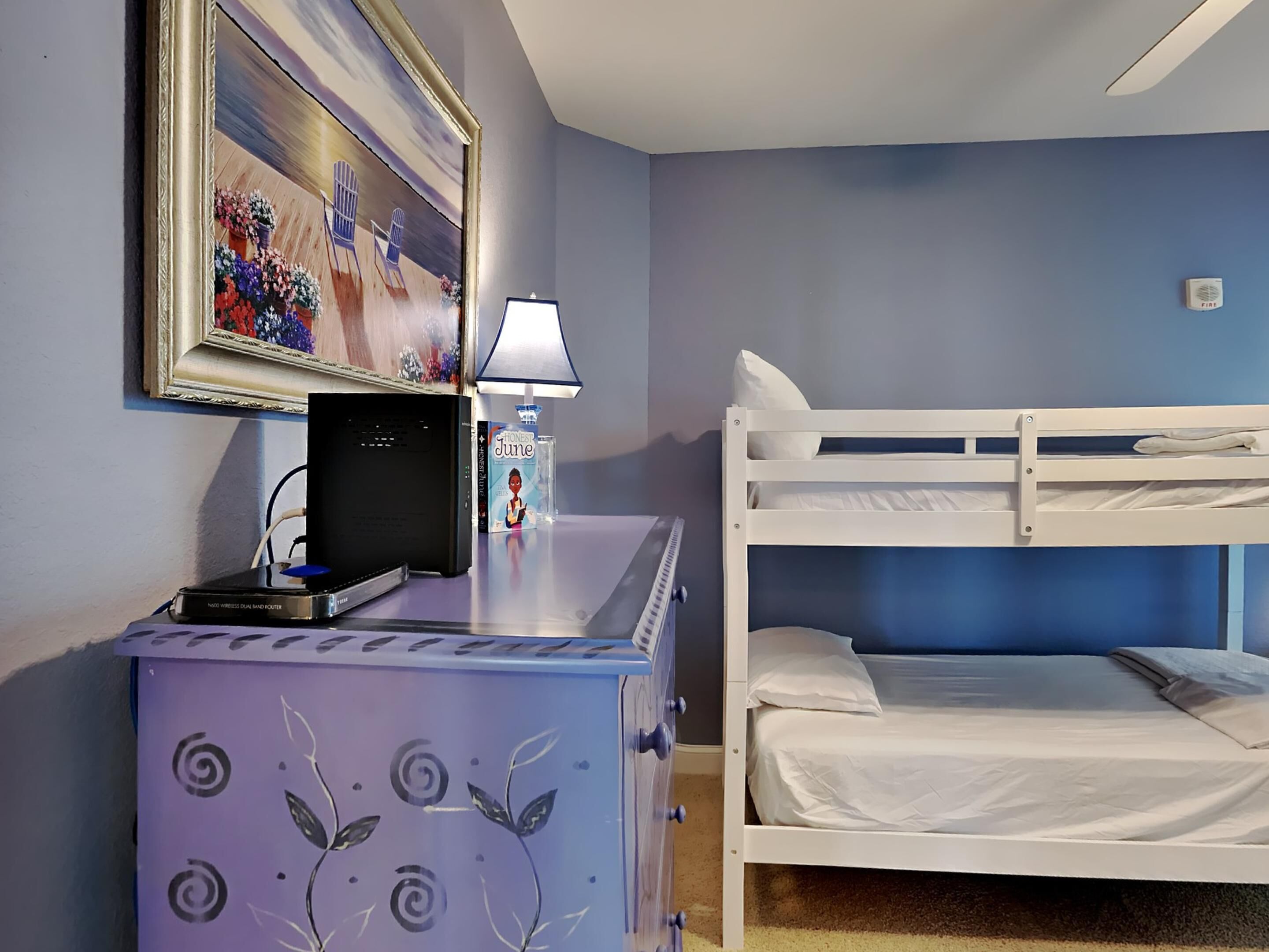 A room with a bunk bed, a desk with a computer, a lamp, and a framed painting.