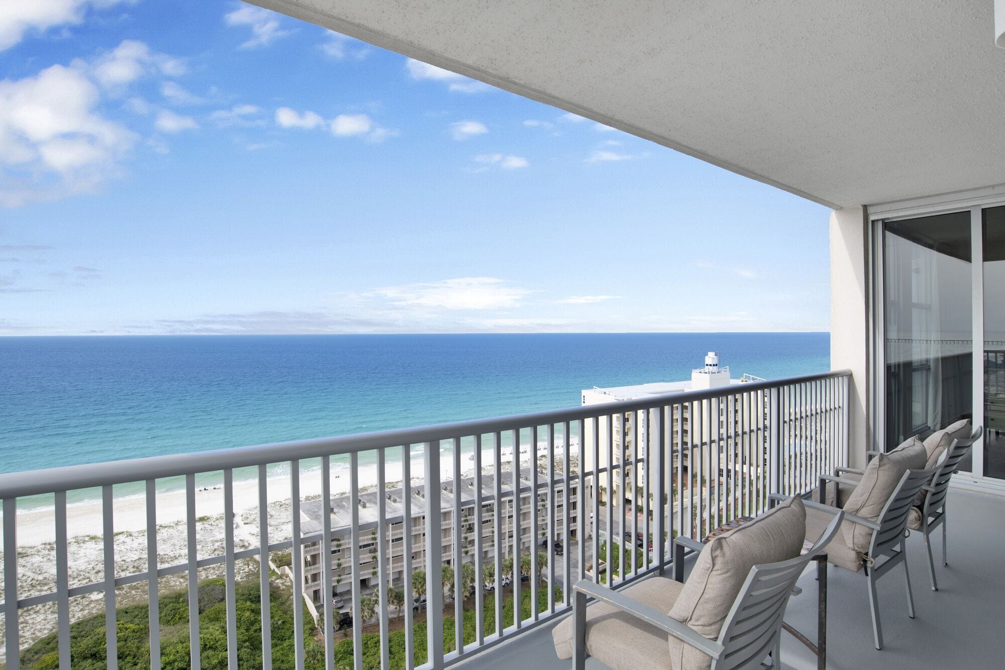 A balcony with a view of the ocean and beach, featuring a seating area with chairs and a table.