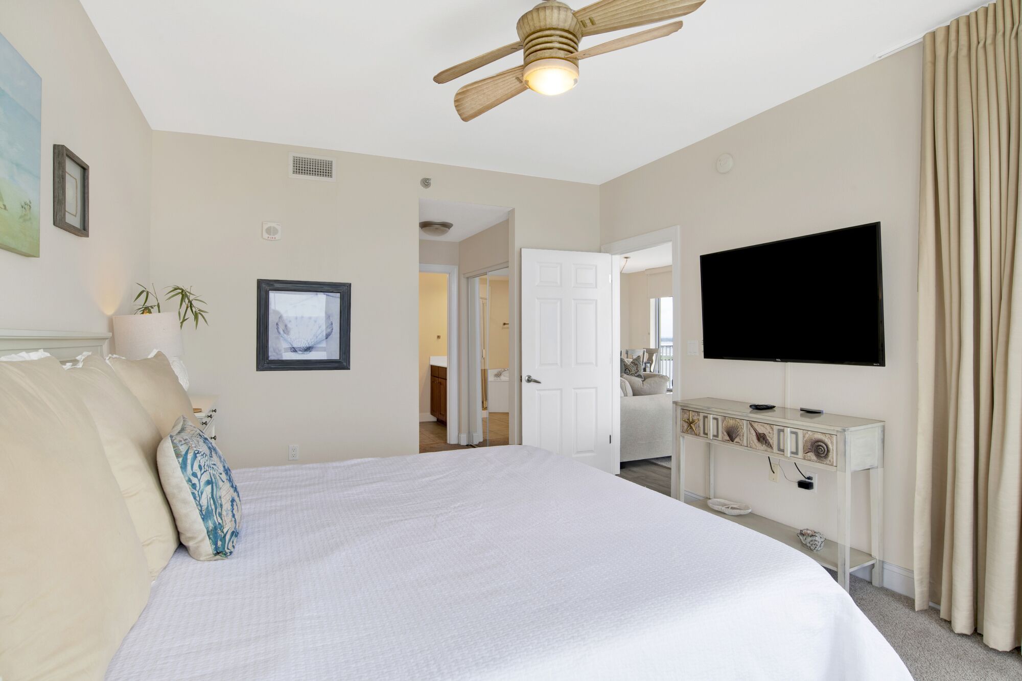 Une chambre d’hôtel avec un grand lit, un ventilateur de plafond, une télévision et une salle de bain visible à travers une porte ouverte.