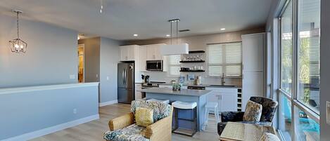 Un amplio salón con cocina, muebles de mimbre y ventanas grandes.
