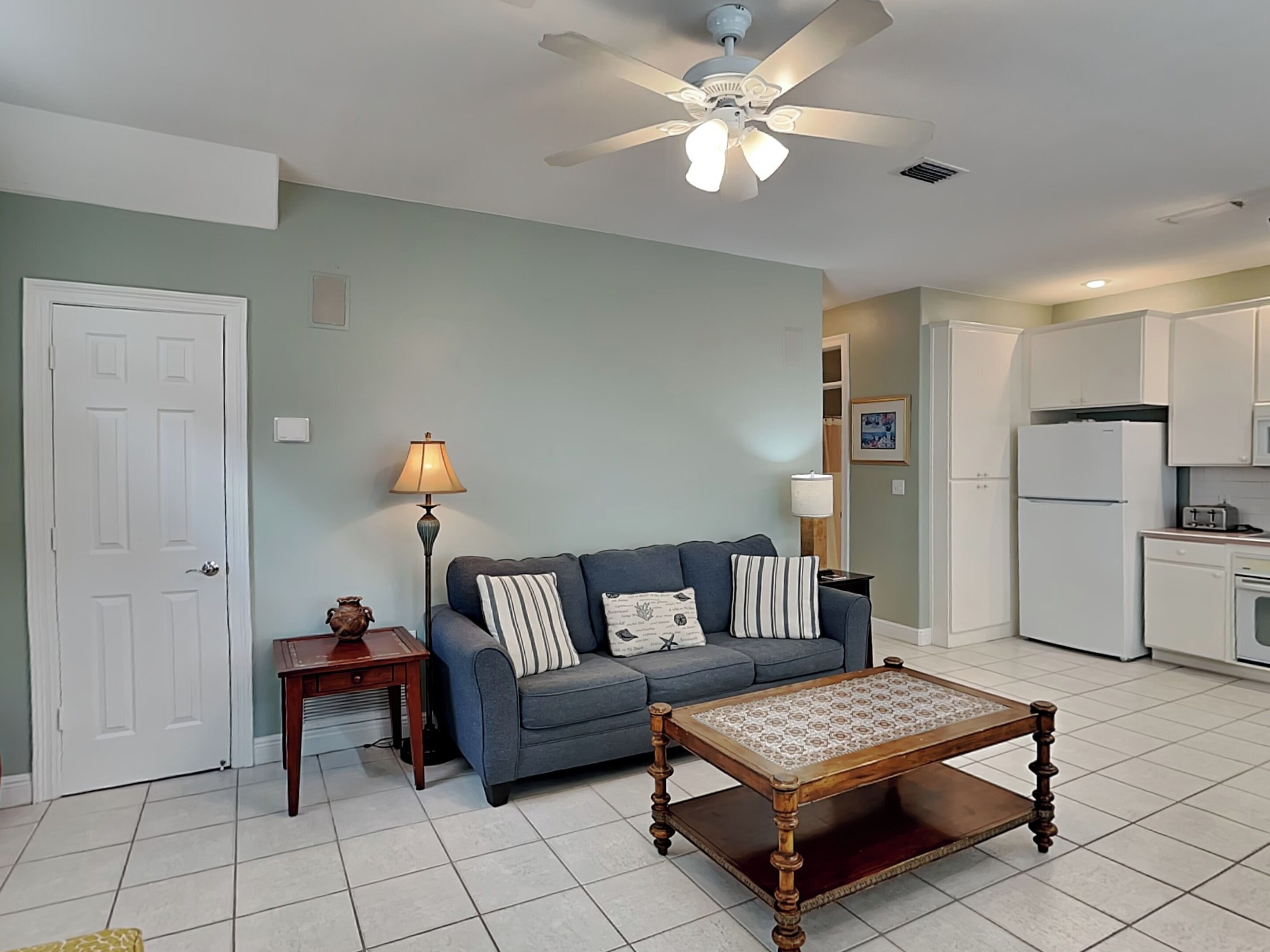 A living room with a sofa, a coffee table, a lamp, and a ceiling fan.
