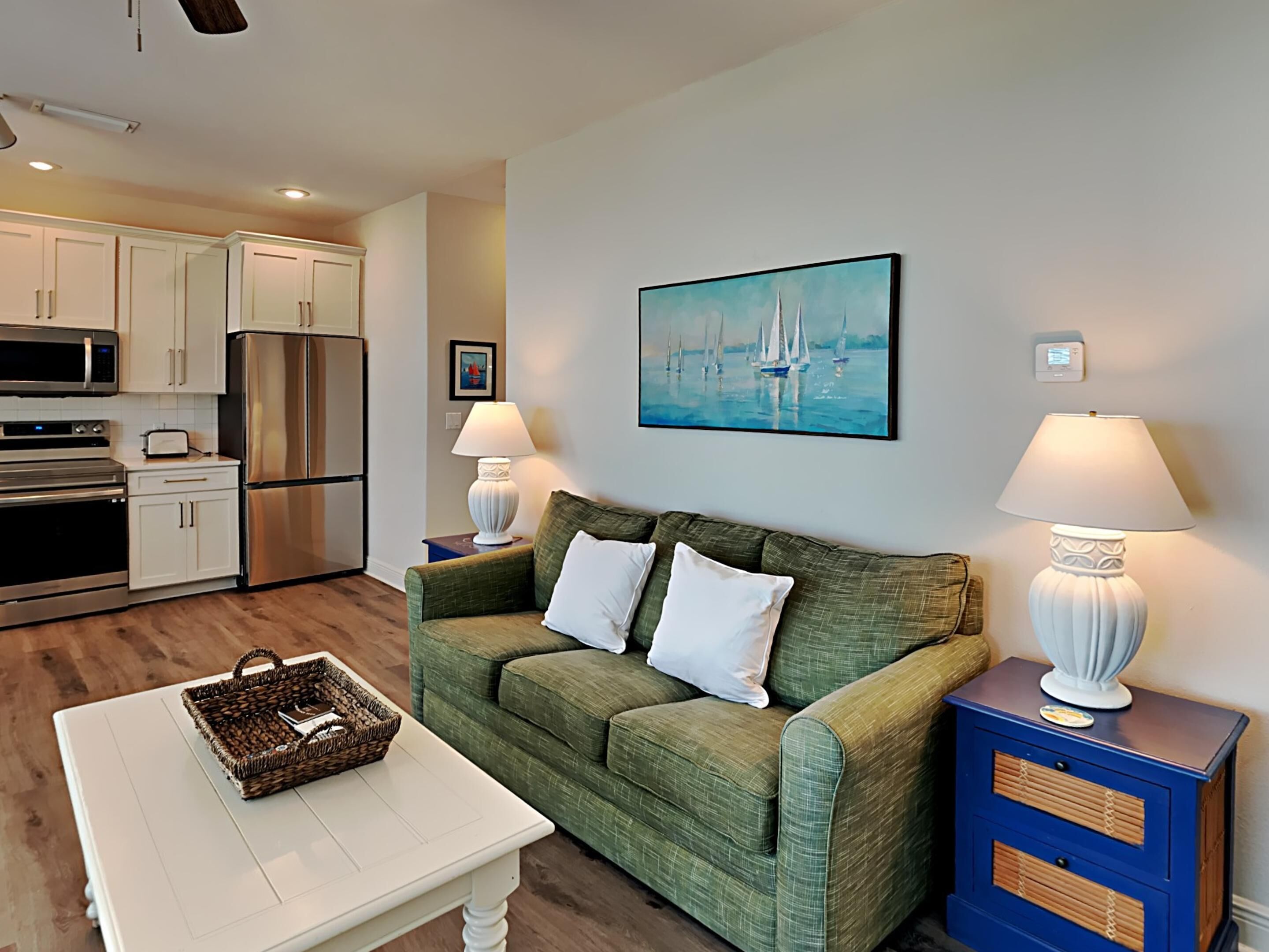 A living room with a green sofa, white cushions, a white coffee table, and a blue side table with a lamp.