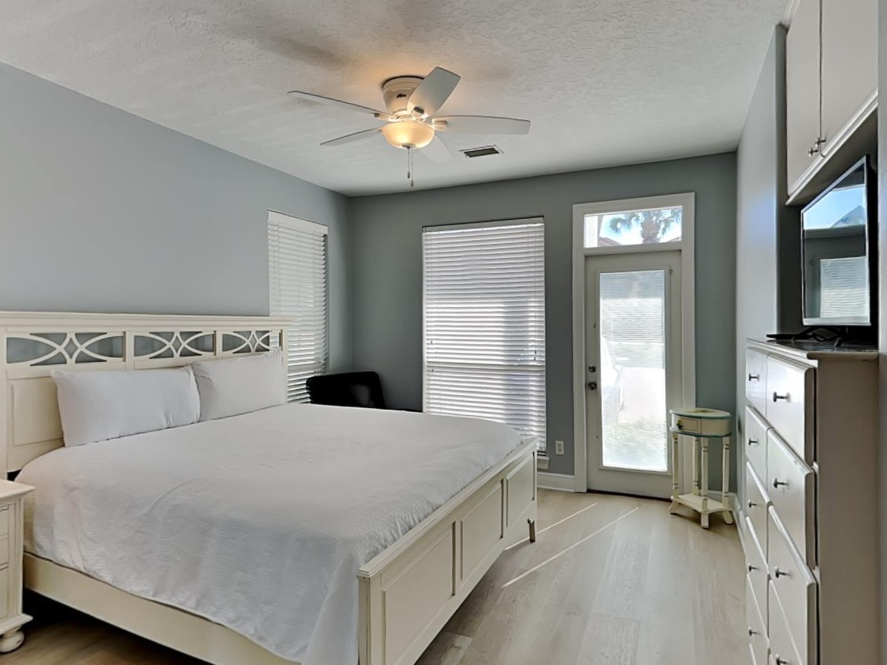 A bedroom with a bed, a ceiling fan, a dresser, and a television.