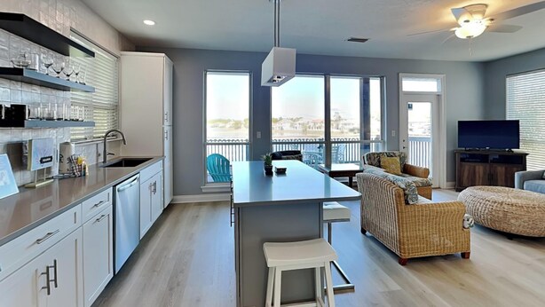 A modern kitchen with a central island, a dining area with a sofa and chairs, and a living room with a TV and a large window offering a view. - Destiny Beach Villas by Southern Vacation Rentals (Destin)
