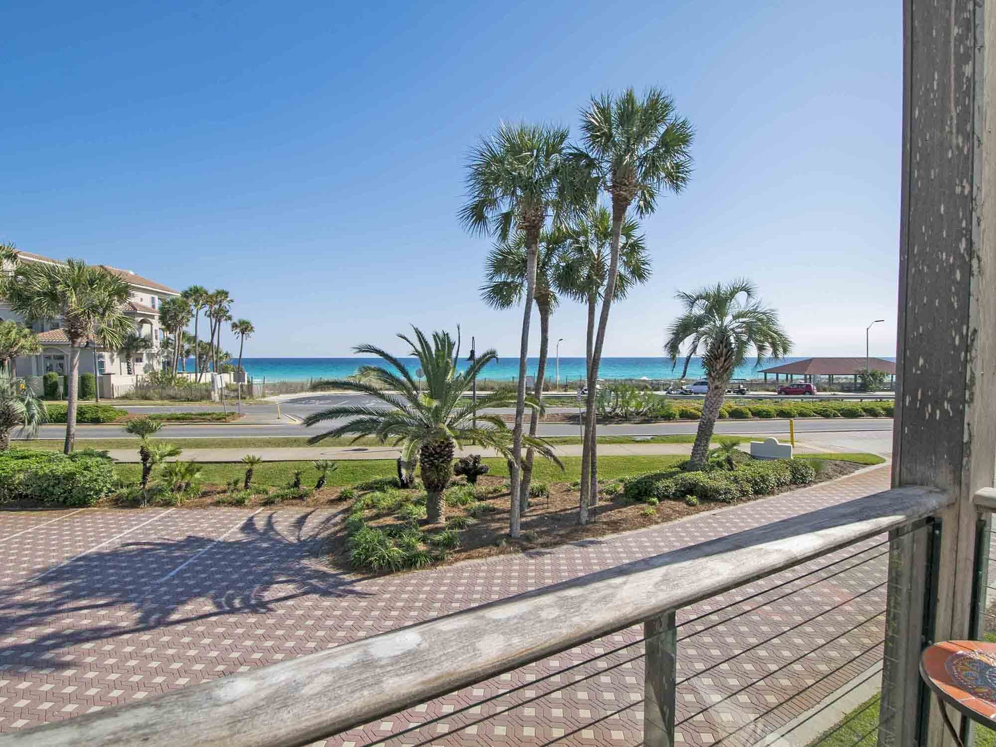 A balcony with a view of the beach, palm trees, and a parking area.