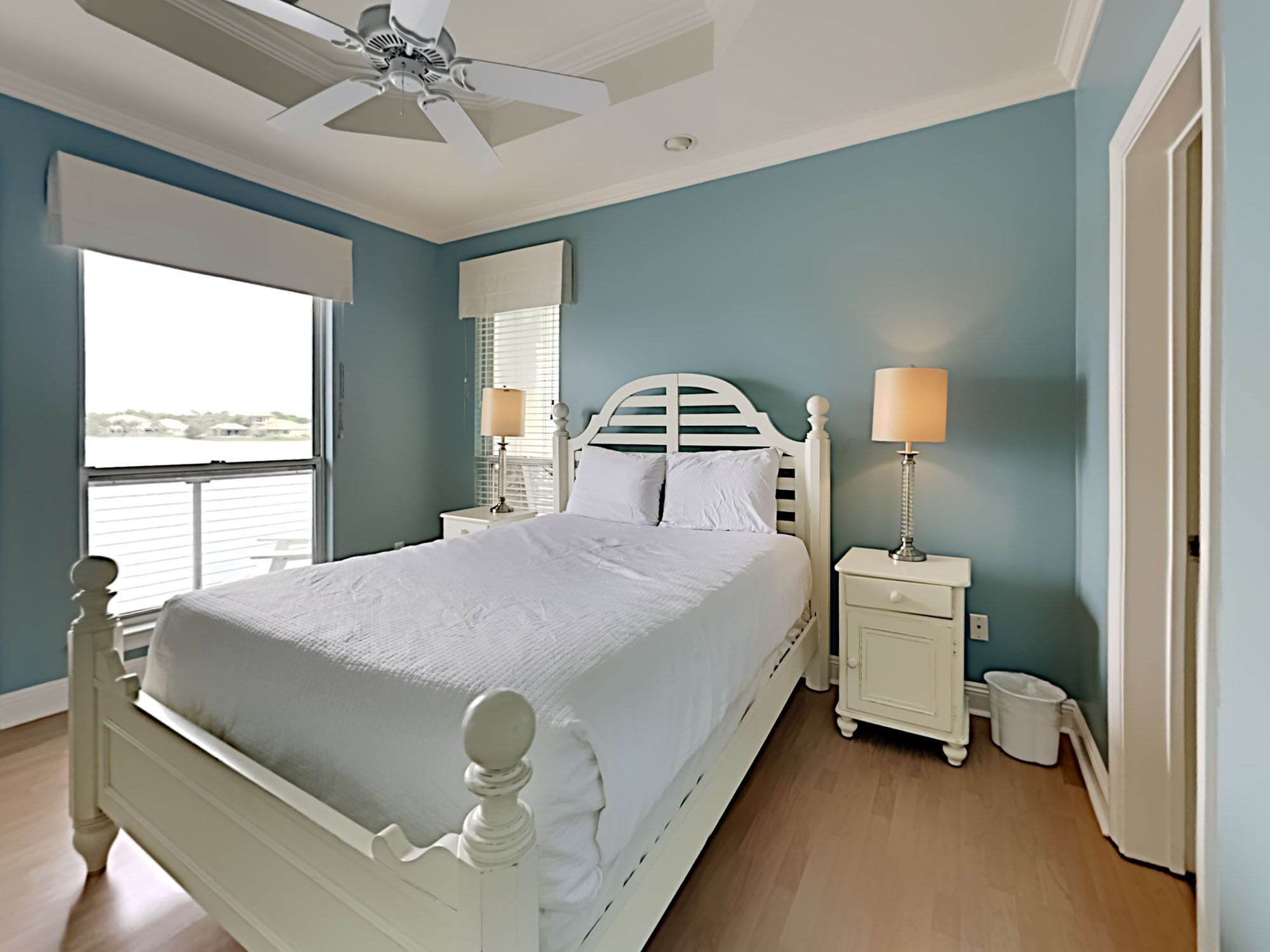 Quarto com cama, mesas de cabeceira, ventoinha no teto e vista para o exterior.