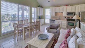 A spacious living area with a dining table, chairs, a sofa, and a kitchen with white cabinets and appliances. - Destiny Beach Villas by Southern Vacation Rentals (Destin)