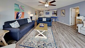 A living room with two sofas, a coffee table, and a rug. There is a ceiling fan and a painting on the wall. - El Matador by Southern Vacation Rentals (Fort Walton Beach)