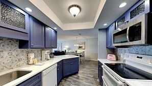 A modern kitchen with blue cabinets, a central island, a microwave, an oven, and a coffee maker. - El Matador by Southern Vacation Rentals (Fort Walton Beach)