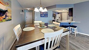 A dining area with a wooden table, white chairs, and a hanging light fixture. - El Matador by Southern Vacation Rentals (Fort Walton Beach)