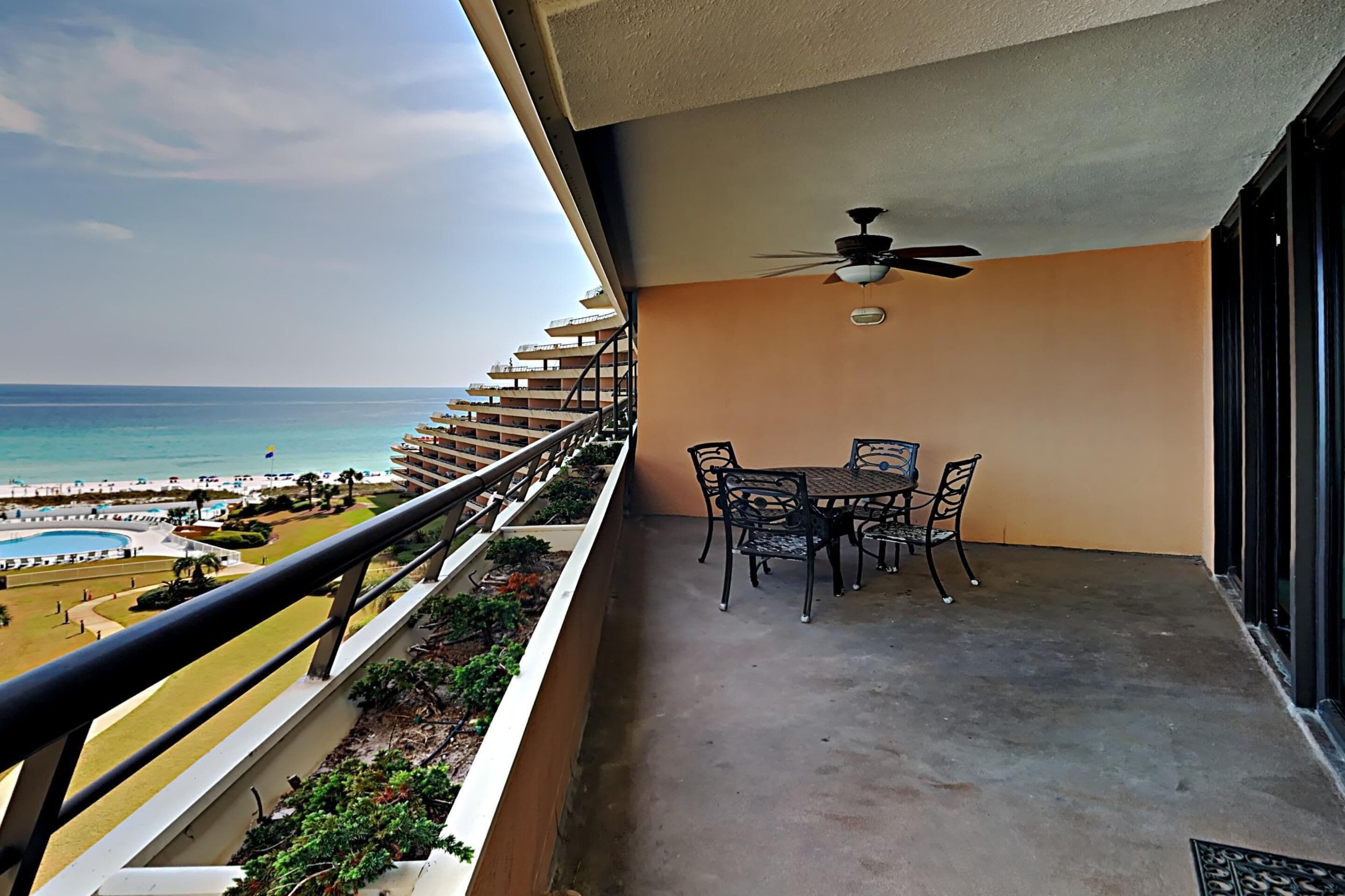 Un balcón con mesa y sillas, un ventilador de techo y vista a la playa y al océano.