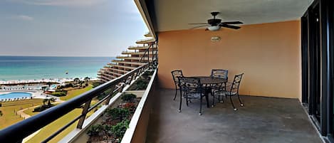 Un balcón con mesa y sillas, un ventilador de techo y vista a la playa y al océano.