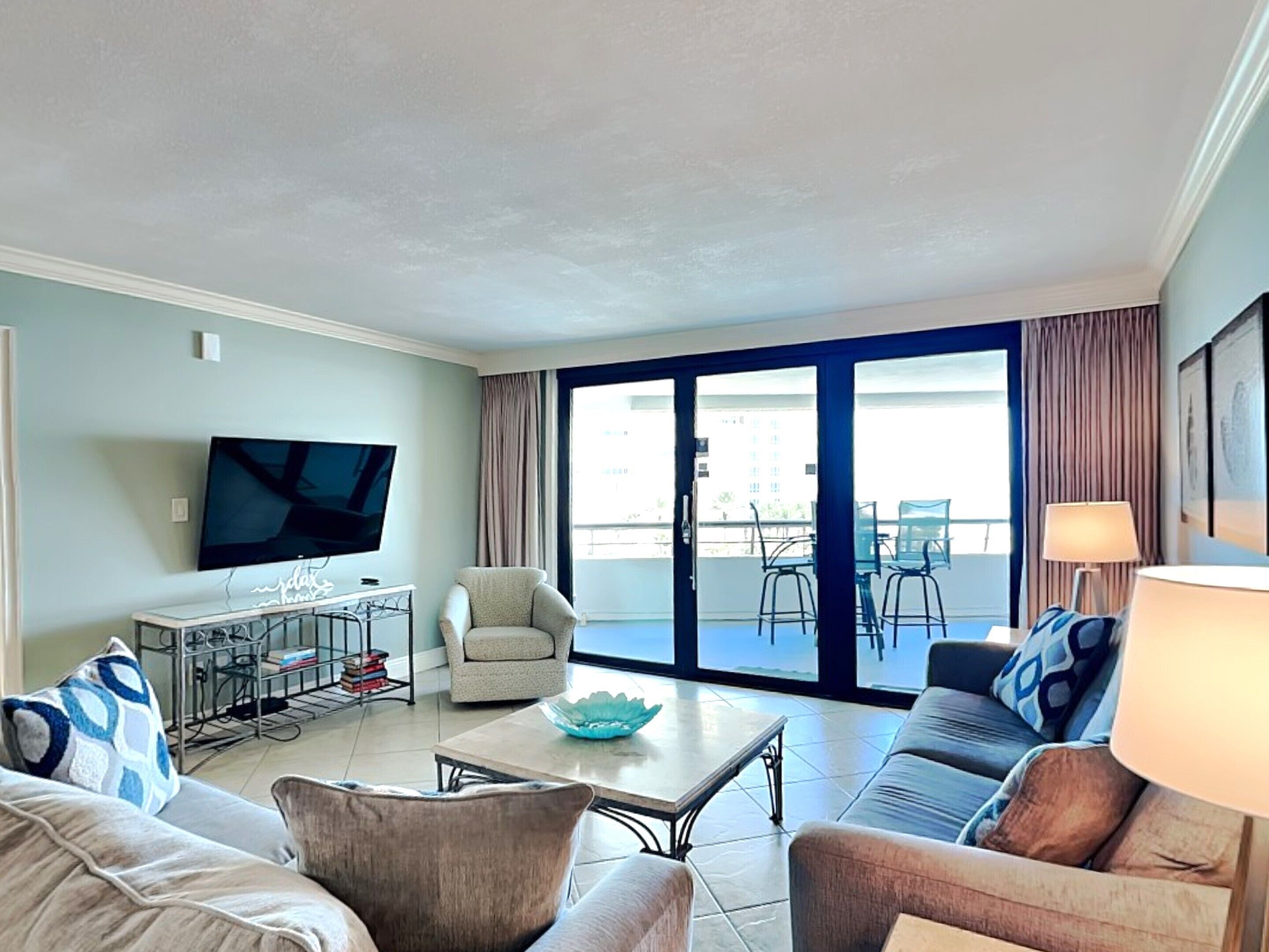 A living room with a television, a sofa, a coffee table, and a balcony with chairs.