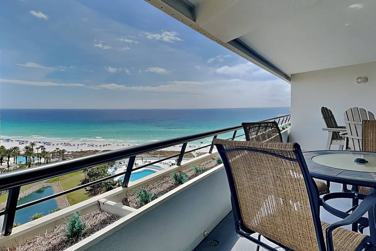 A balcony with a view of the beach and ocean, wicker chairs, and a small table.