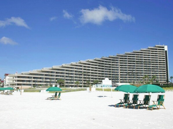 A large hotel with multiple balconies, a sandy beach in the foreground, and green umbrellas. - Edgewater by Southern Vacation Rentals (Miramar Beach)