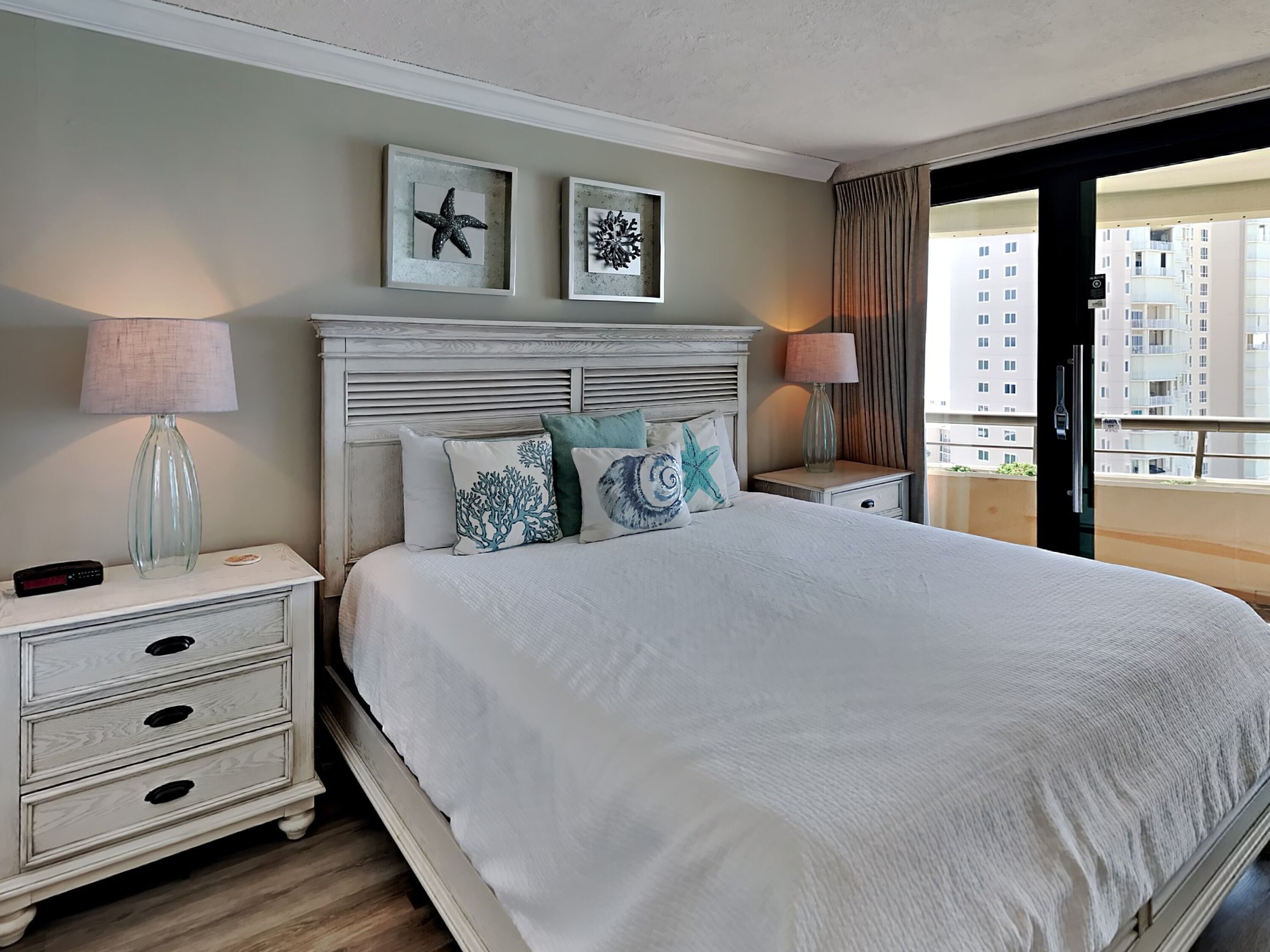 Habitación de hotel ordenada con una cama grande, dos mesitas de noche, una lámpara y cuadros en la pared.