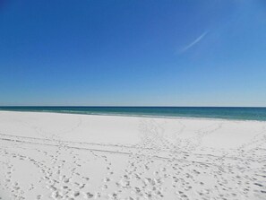 A wide, white sandy beach with footprints leading to the water.