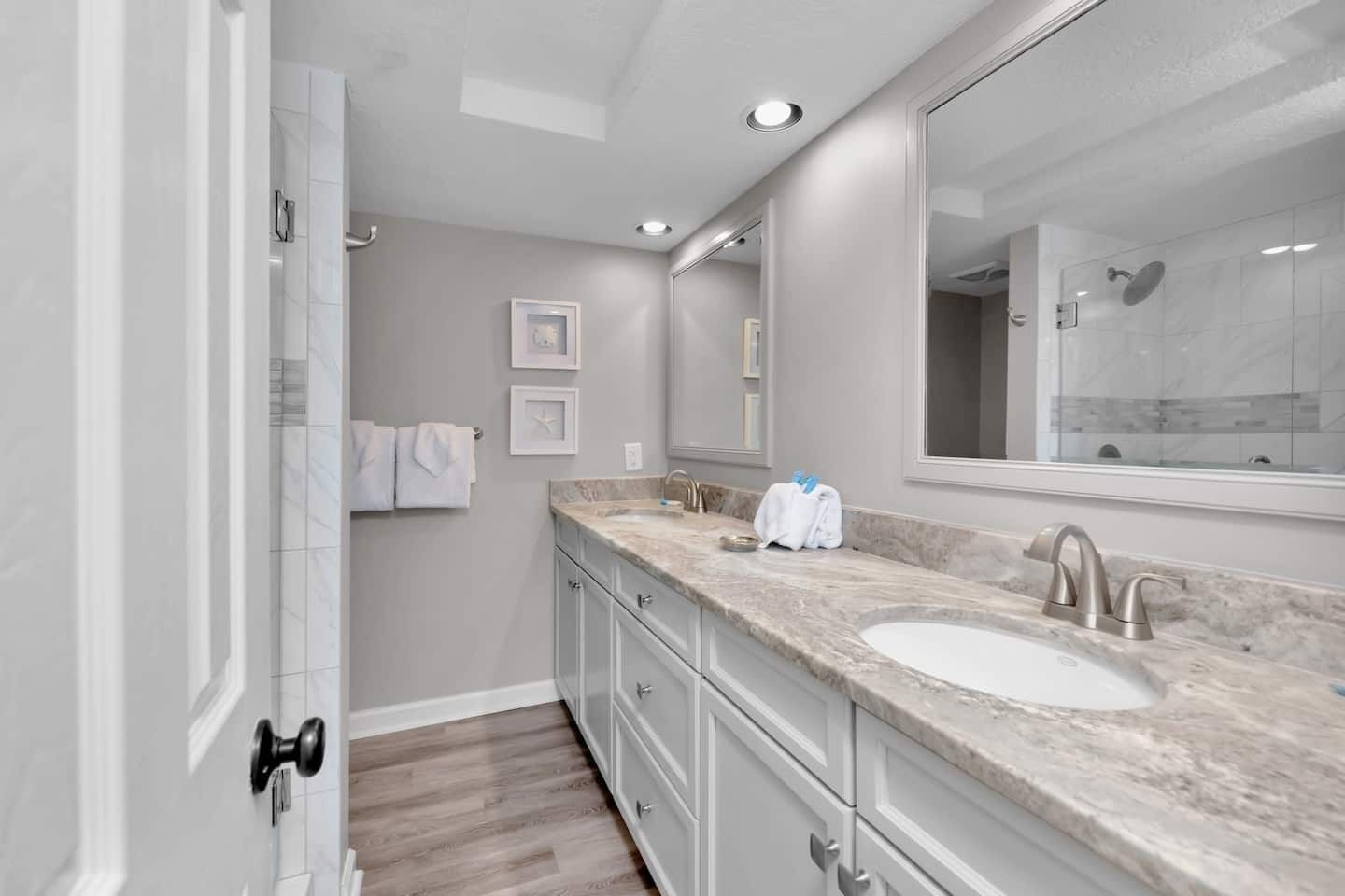 A modern bathroom with a large mirror, two sinks, and a shower.