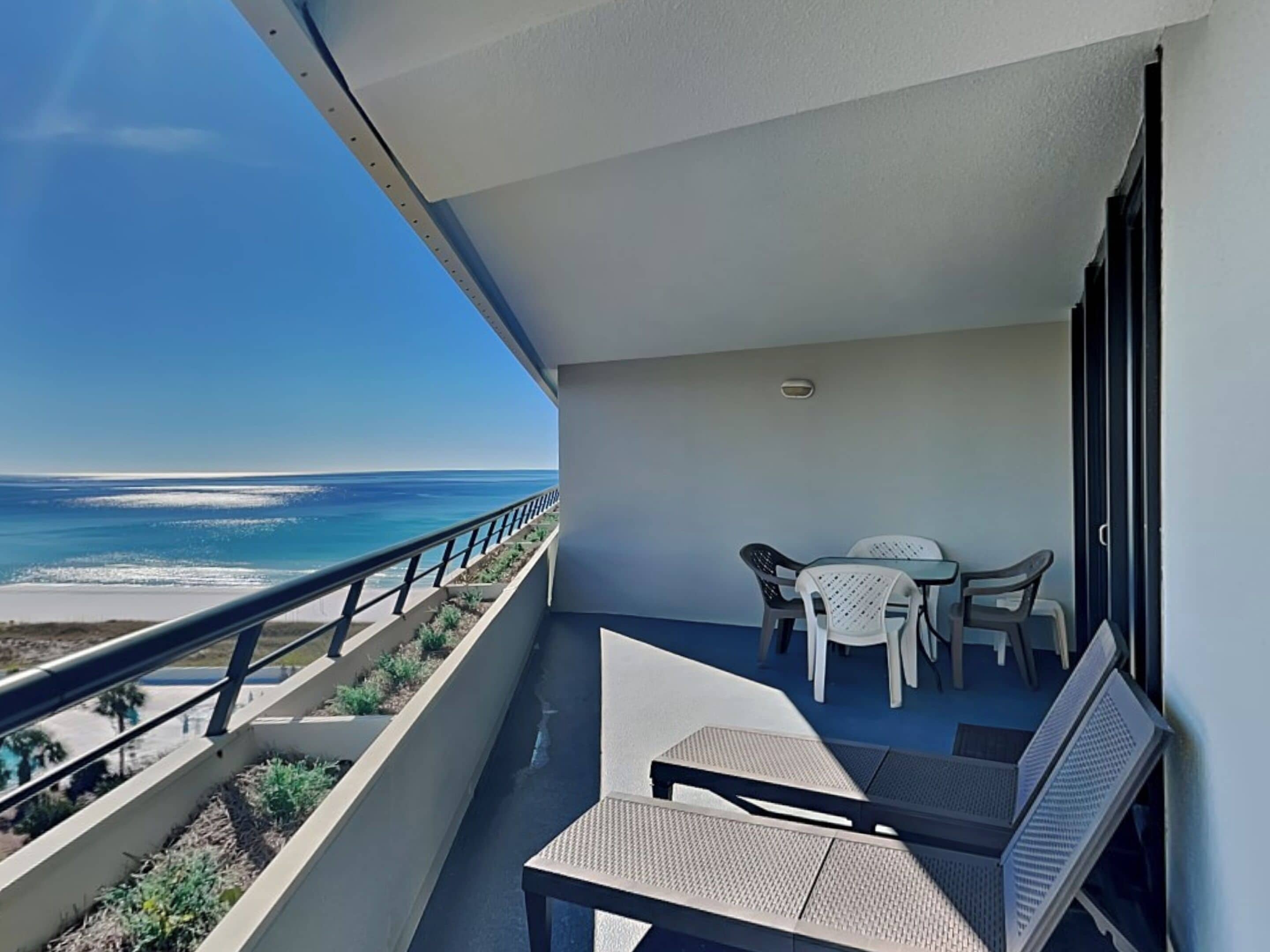A balcony with a view of the ocean, a table with chairs, and a bench.