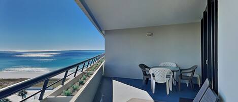 A balcony with a view of the ocean, a table with chairs, and a bench.