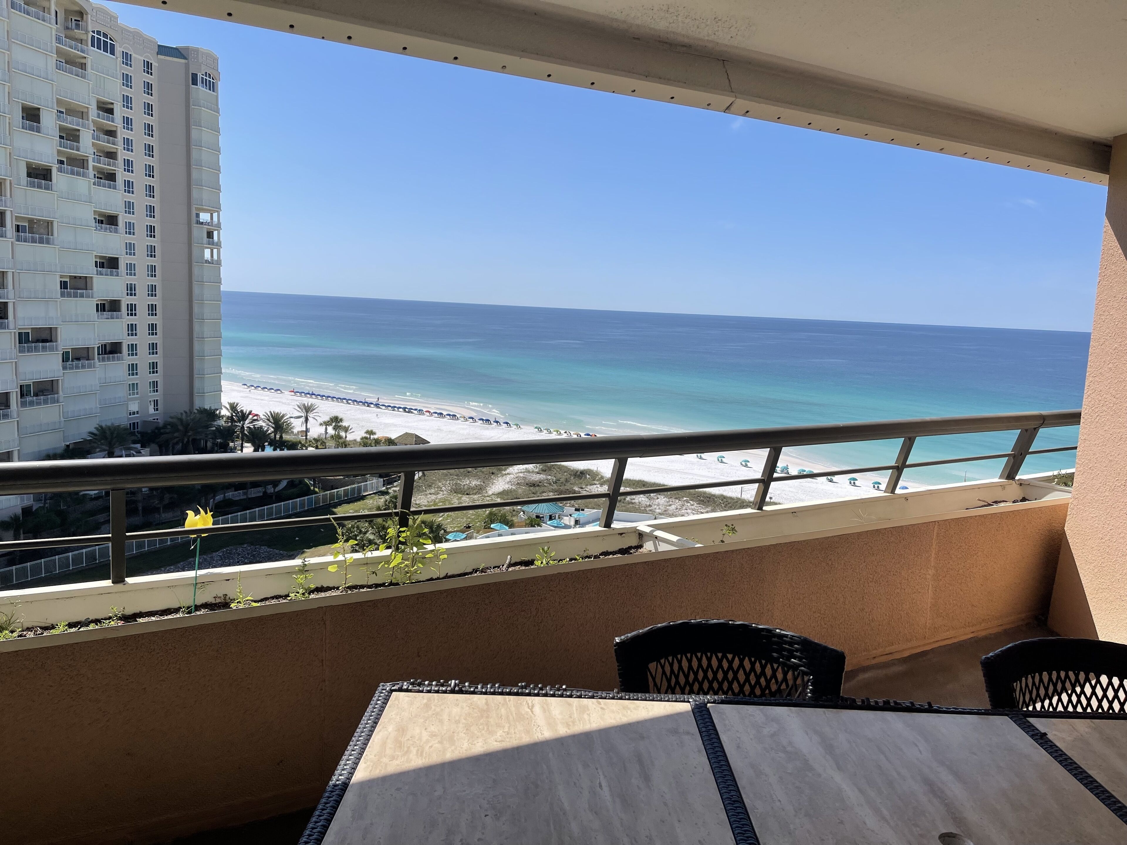 A balcony with a view of a beach and ocean, a dining table, and chairs.