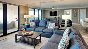 A modern living room with a large sectional sofa, a coffee table, and a TV. There is a sliding glass door leading to an outdoor area. - Edgewater by Southern Vacation Rentals (Miramar Beach)