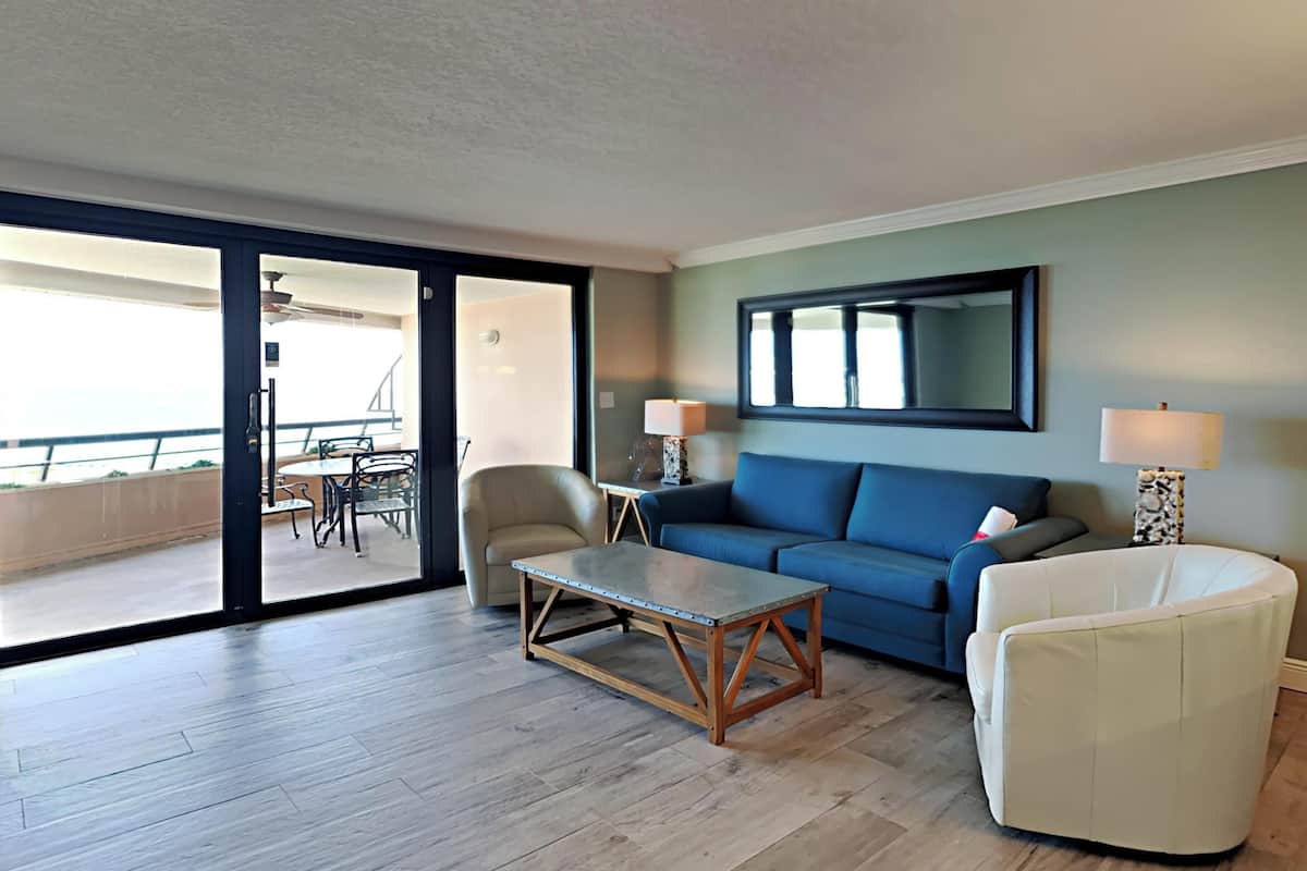 A living room with a sofa, a coffee table, a chair, and a large window.