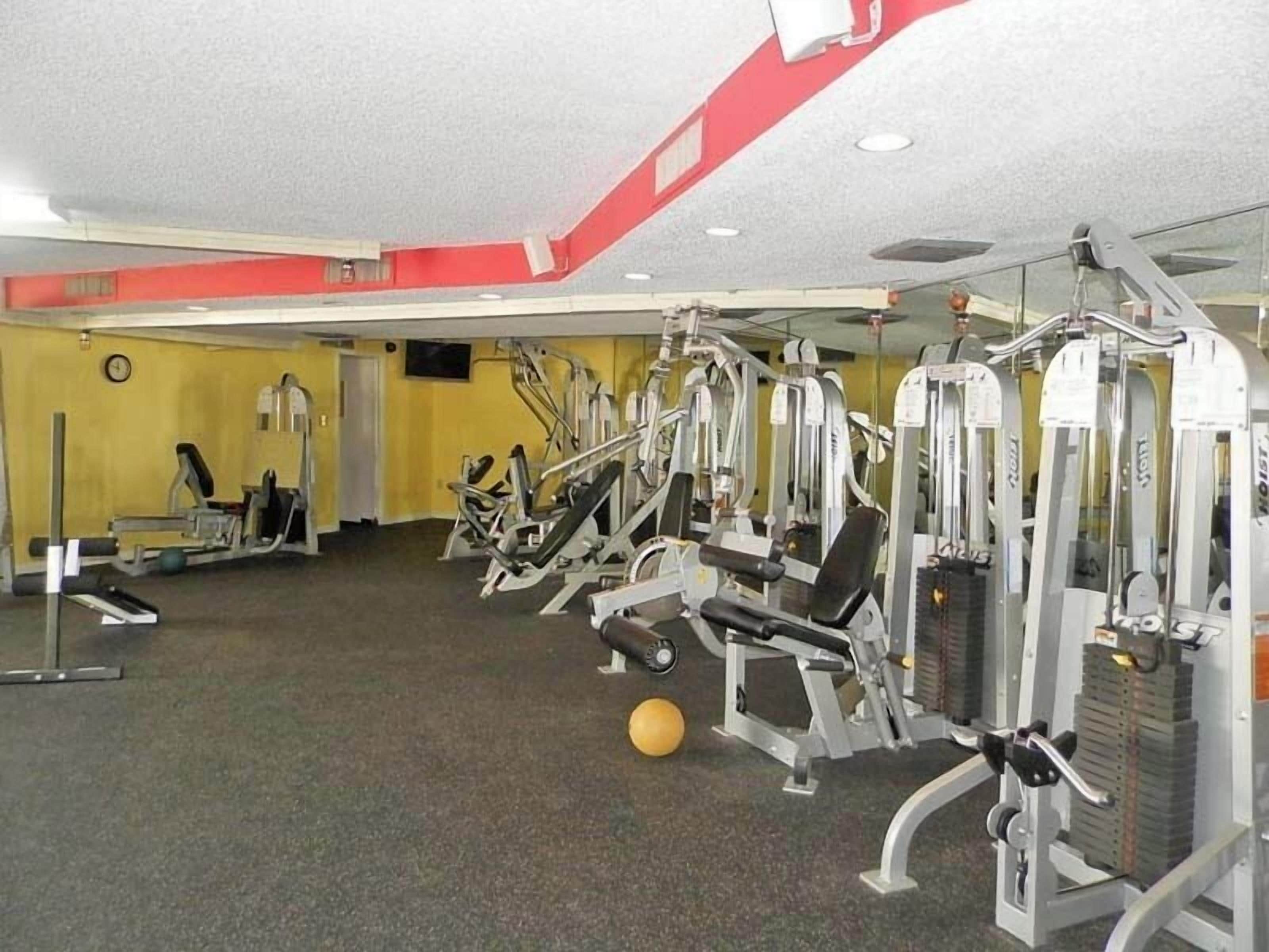 A gym with various exercise machines, a clock on the wall, and a yellow wall.