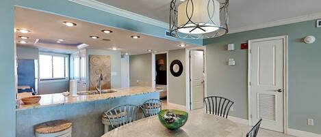 A modern kitchen with a central island, a dining table with chairs, and a ceiling light fixture.