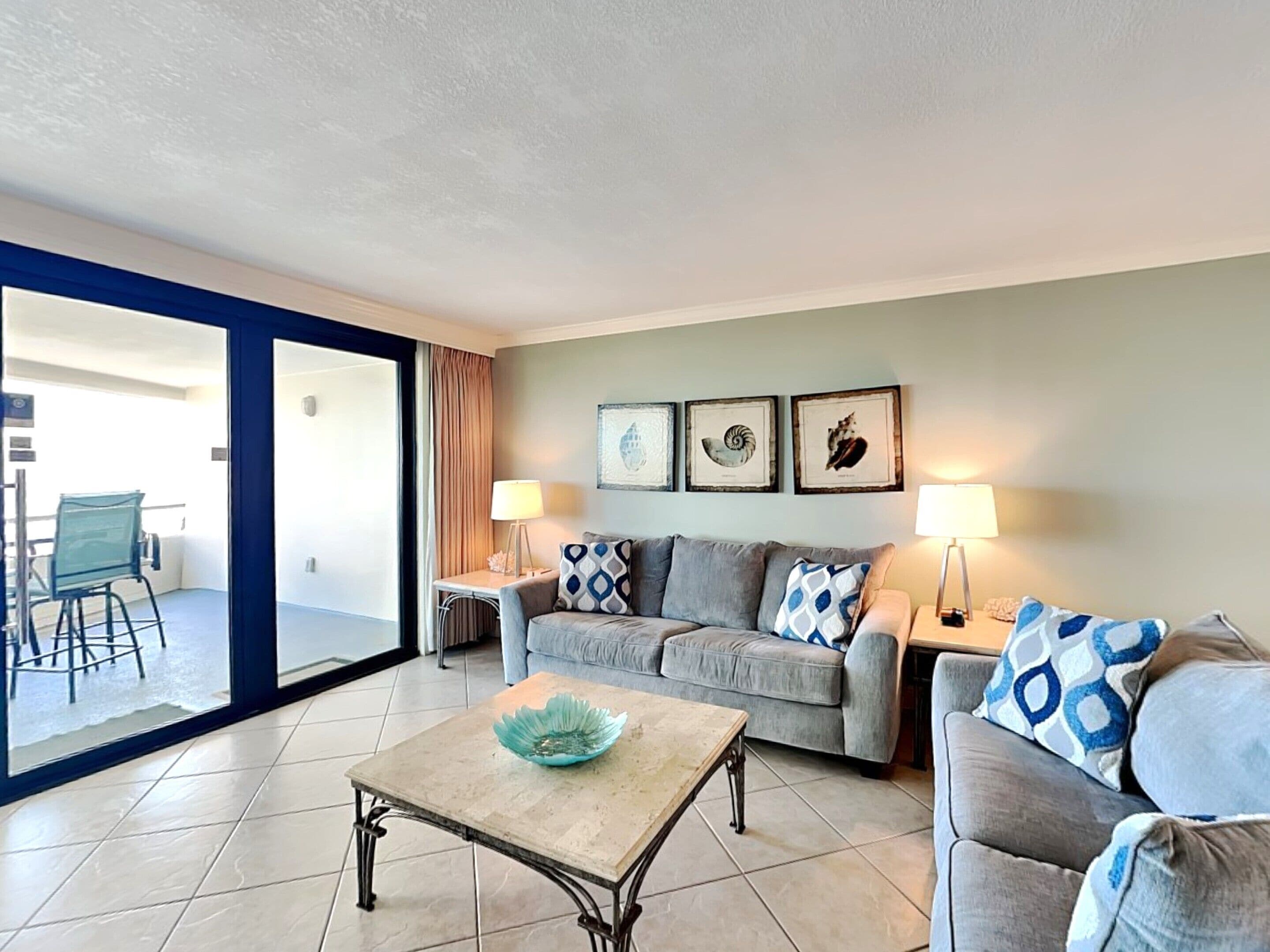 A living room with a sofa, two side tables, a coffee table, and a view of the outside.