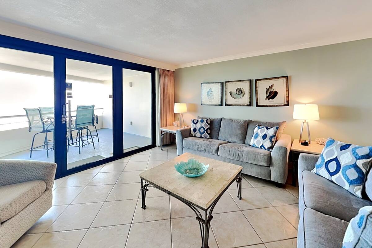 A living room with a sofa, armchairs, a coffee table, and a balcony with chairs.