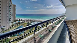 A balcony with a view of a beach, a pool, and a tall building. - Edgewater by Southern Vacation Rentals (Miramar Beach)