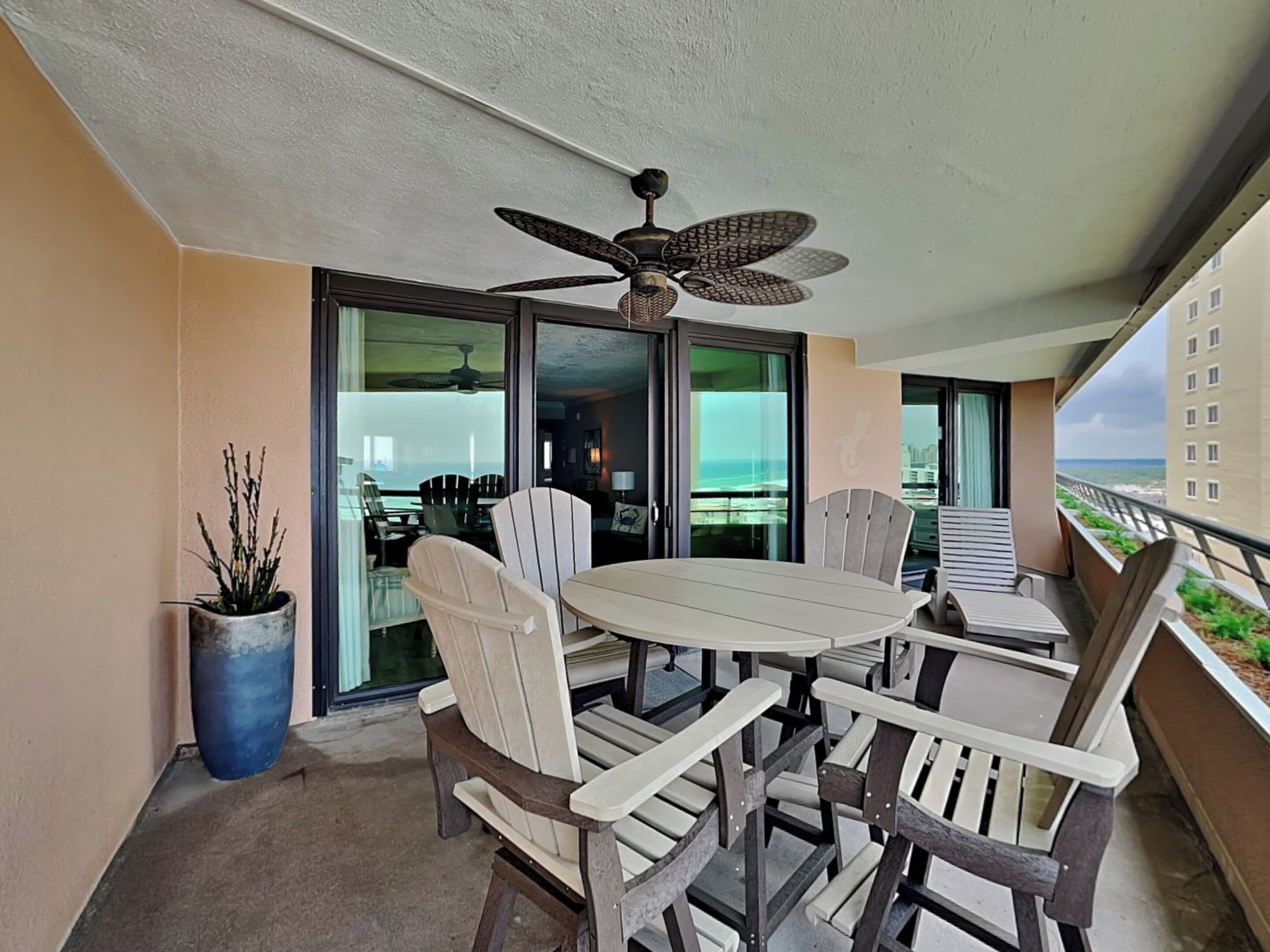 Een balkon met een tafel en stoelen, een plafondventilator en uitzicht op de oceaan.