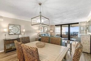 A spacious living area with a large wooden table, comfortable seating, a chandelier, and a balcony with a view. - Edgewater by Southern Vacation Rentals (Miramar Beach)